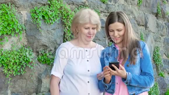 年长的女人和漂亮的年轻女孩使用智能手机背景中野生石头的复古墙视频的预览图