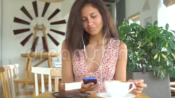 女孩用耳机在智能手机上听音乐喝咖啡视频的预览图
