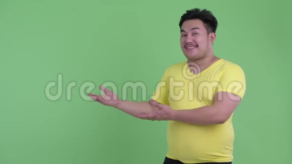 快乐的年轻超重的亚洲男人一边说话一边展示视频的预览图