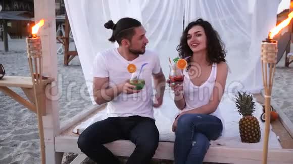 一对夫妇在海滩上喝彩色鸡尾酒一个异国情调的假期鸡尾酒会海滩上的平房背景热带视频的预览图