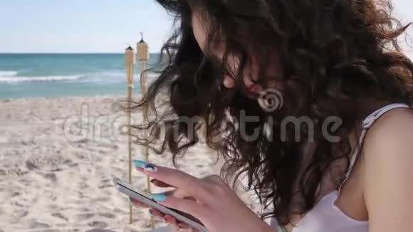暑假用手机交流女孩用小工具浏览社交网络沙滩上的年轻女子视频的预览图