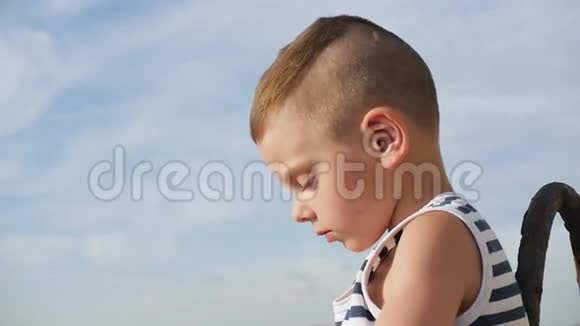 快乐的小男孩穿着水手条纹衬衫在天空和大海的背景下玩耍视频的预览图