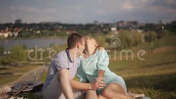 年轻的恋人们在公园的绿草上休息以城市为背景视频的预览图