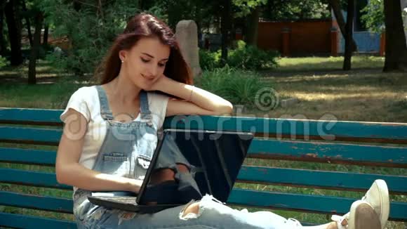 微笑着躺在长凳上的年轻女士拿着笔记本电脑视频的预览图