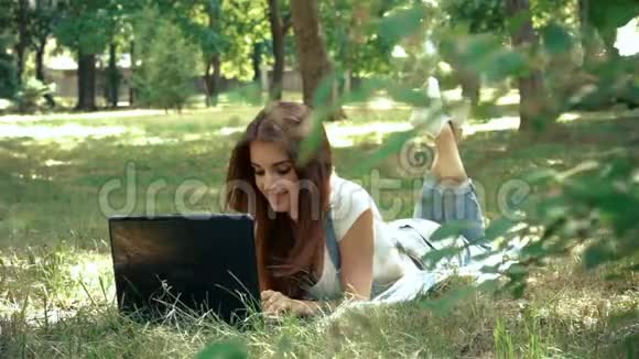 迷人的女士穿着笔记本电脑躺在绿草上视频的预览图