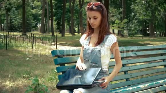 公园里坐着一个带眼镜的迷人少女打开笔记本电脑视频的预览图