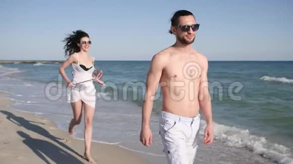 情侣在沙滩上拍自拍照片男人围着女孩转积极的年轻人从假期旅行中拍摄视频视频的预览图