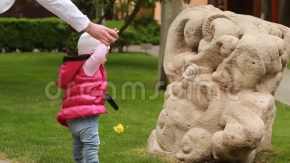 妈妈学着可爱的女婴去草地上的城市公园视频的预览图