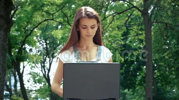 女孩坐在街上微笑着看着笔记本电脑和指纹视频的预览图
