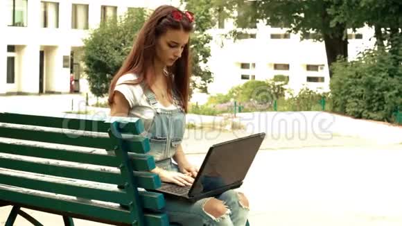 公园里漂亮的时尚女士手提电脑坐在长凳上视频的预览图