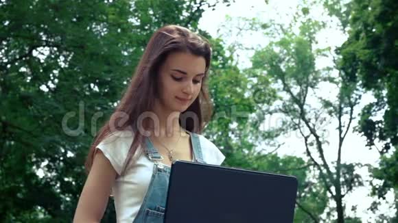 夏天微笑可爱的女孩坐在街上穿着笔记本电脑视频的预览图