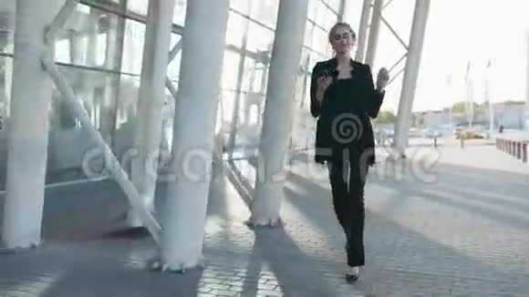 一个自信的年轻金发女孩穿着一套优雅的正式黑色西装走在机场候机楼旁用她视频的预览图