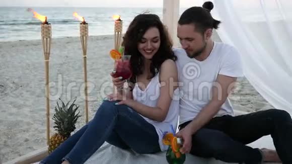 浪漫的夏季假期情侣们热带夫妇带鸡尾酒在海滩平房与白色的乐趣视频的预览图