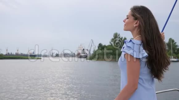 年轻的女性挥手向朋友问好长发在河的背景上的女孩女士站在水边视频的预览图
