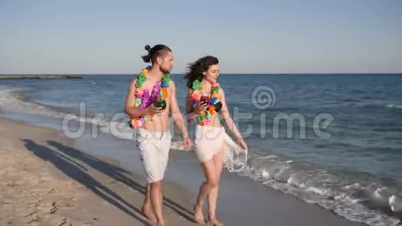 光着脚走在沙滩上情侣们喝着彩色鸡尾酒夏威夷浪漫之旅幸福的人们走在沙滩上视频的预览图