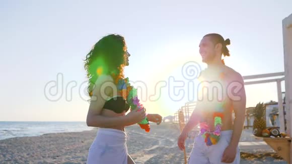 海滩派对到海滨慢动作暑假在海岸恋爱花圈在年轻夫妇的脖子上视频的预览图