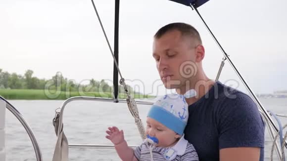 父母带着孩子在户外爸爸抱着儿子在游艇上父亲和小男孩嘴里放着奶嘴视频的预览图