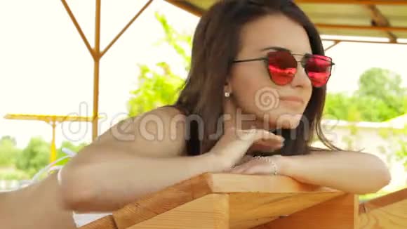 美丽的年轻女子戴着明亮的粉红色眼镜躺在海滩上视频的预览图