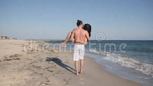 快乐的一对男人抱着女人快乐的朋友在浪漫的散步年轻人在美丽的海滩男人和女孩到夏天视频的预览图