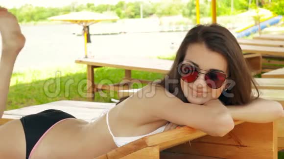 漂亮的年轻黑发女郎戴着眼镜和泳衣躺在海滩休息室里视频的预览图