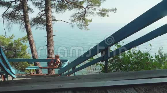年轻的金发白种人嬉皮士女孩在蓝色海洋背景的木码头视频的预览图