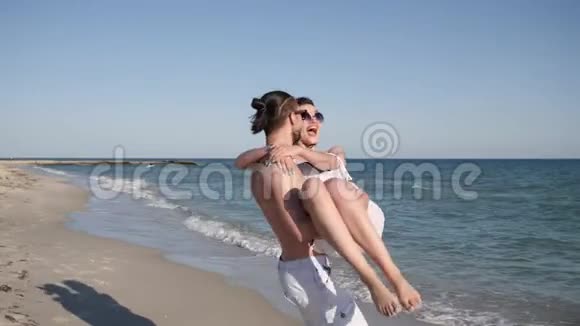 男人在沙滩上抱着女孩年轻人赤着脚在沙滩上散步情侣在异国情调的度假中背景是视频的预览图