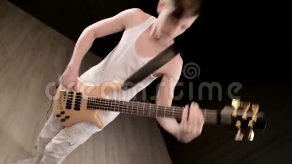 年轻的男音乐家穿着白色的衣服黑色背景上有一把米色的低音吉他低音吉他演奏者演奏音乐视频的预览图