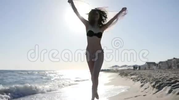 女人在背光下的海滩上奔跑慢动作穿着泳衣背景沙子和大海的快乐女孩沿着海滩奔跑视频的预览图