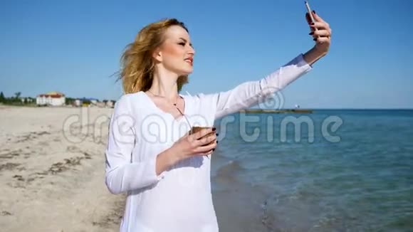 女孩在海滩上自拍手里的手机在海边拍度假照片视频的预览图