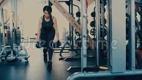 多年来漂亮的运动型的黑发女人在健身房里用哑铃做运动视频的预览图
