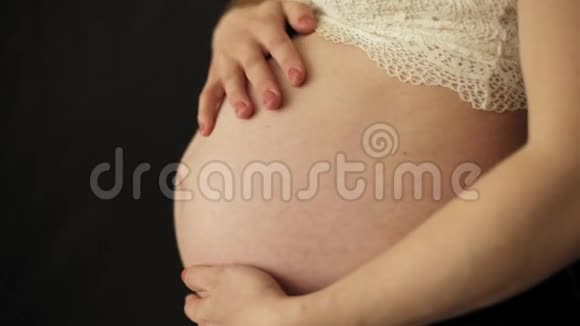 孕妇抚摸着她赤裸的大肚子贴在黑色的背景上视频的预览图