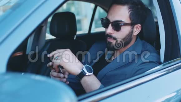 英俊的留胡子男人戴着时髦的太阳镜坐在商务舱里拿着电话信息微笑着视频的预览图