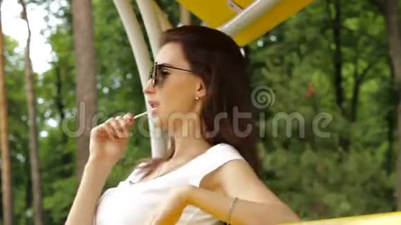 戴眼镜的时髦女孩舔着棒棒糖坐在秋千上视频的预览图
