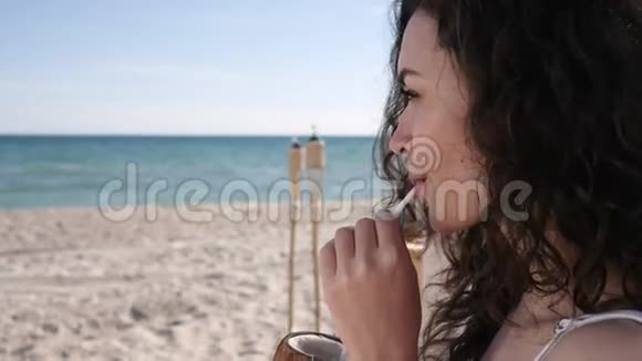 肖像可爱的女孩卷发喝鸡尾酒吸管N夏季背景海洋和沙子视频的预览图