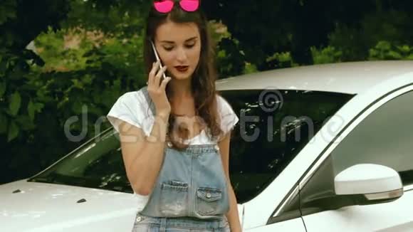 美丽的女孩站在车旁边用手机说视频的预览图