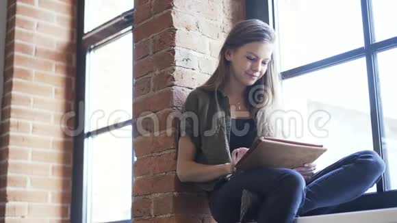在窗台上微笑着拿着平板电脑的年轻女子平底锅视频的预览图