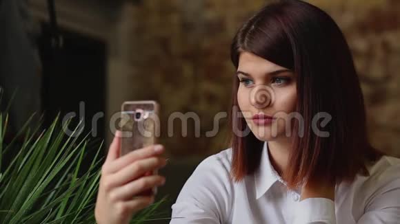 咖啡馆里微笑的女孩一边喝咖啡一边用智能手机聊天视频的预览图