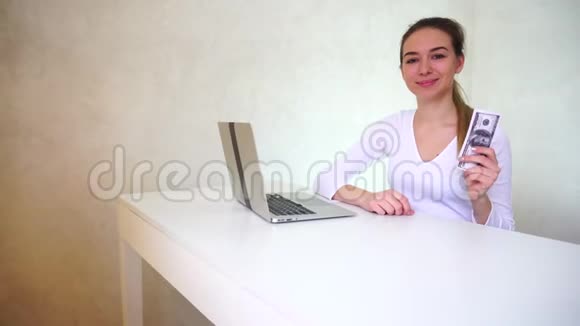 女人得到了贷款可爱的坐在桌旁手提电脑还在相机上吹牛视频的预览图