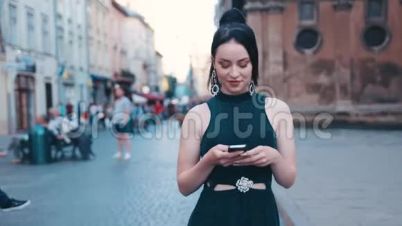 迷人的年轻女子穿着休闲的黑色连衣裙和美丽的马尾辫走在历史市中心并使用视频的预览图