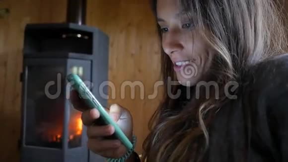 年轻迷人的混合种族妇女微笑和使用移动电话附近的壁炉舒适和科技高清慢速运动视频的预览图