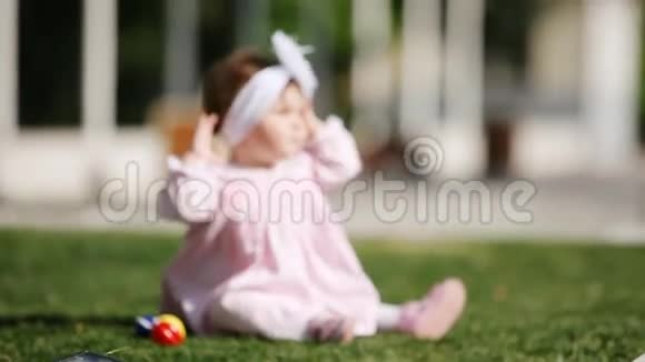 快乐的女婴坐在公园的绿草上玩着模糊的形象视频的预览图
