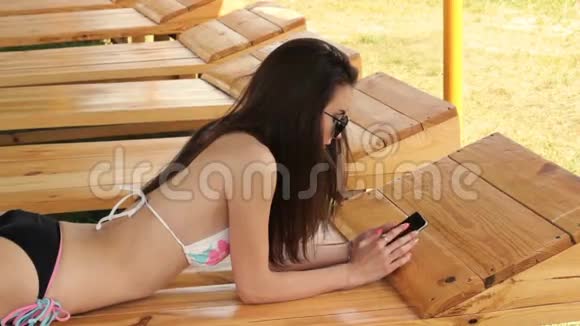 穿着泳衣的漂亮女士躺在海滩上看着你的手机视频的预览图