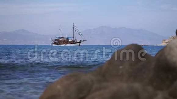 老式船帆停泊在海里波浪撞击前景的石头视频的预览图