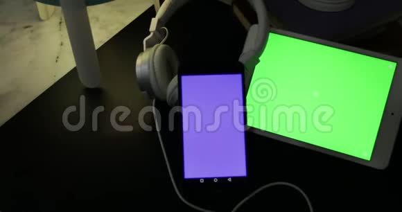 晚上在桌上放带耳机的蓝屏手机和绿屏平板电脑视频的预览图