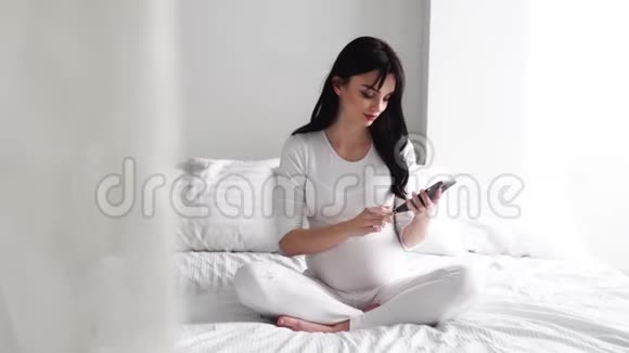 带手机的孕妇在卧室的床上视频的预览图