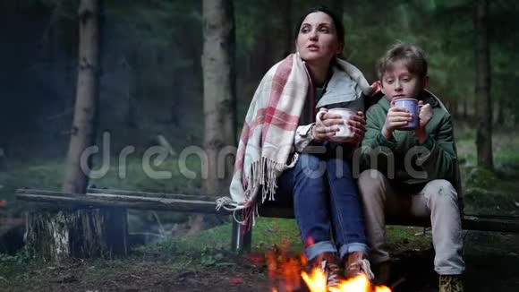 母亲和儿子一起喝茶在森林篝火附近聊天视频的预览图