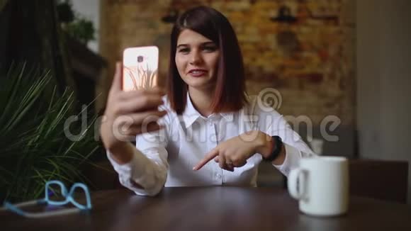咖啡馆里微笑的女孩一边喝咖啡一边用智能手机聊天视频的预览图