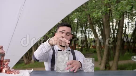 酒吧管理员在大自然中搅拌冰块在酒吧柜台上放冰块的玻璃杯酒吧管理员将饮料冷却到视频的预览图