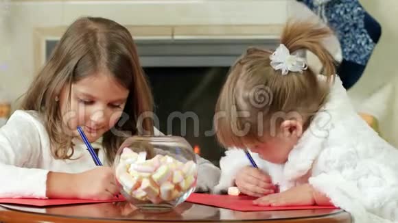 孩子们在一张纸上画一支笔两个女孩写字可爱的孩子坐在火炉旁视频的预览图