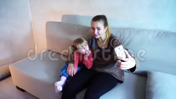 美国血统的年轻母亲和小女儿坐在沙发上打电话拍照视频的预览图